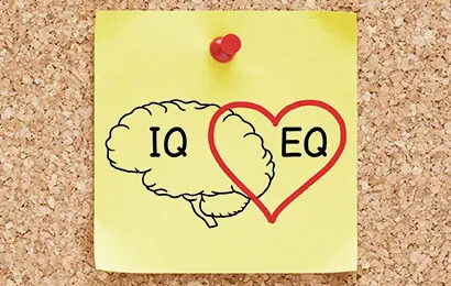 A yellow sticky note pinned to a corkboard shows a drawing of a brain labeled "IQ" and a red heart shape labeled "EQ" overlapping the brain.